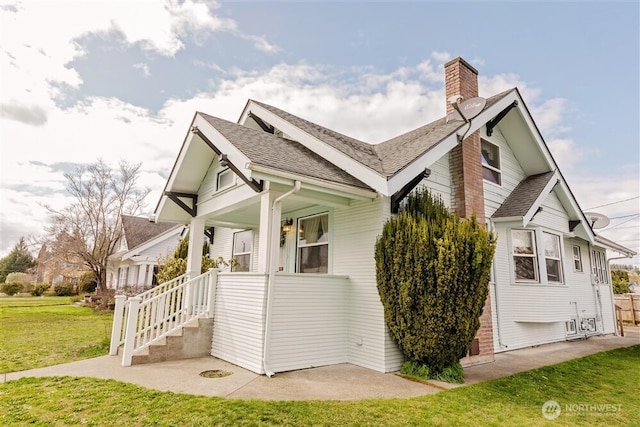 view of home's exterior featuring a chimney, a porch, roof with shingles, and a lawn