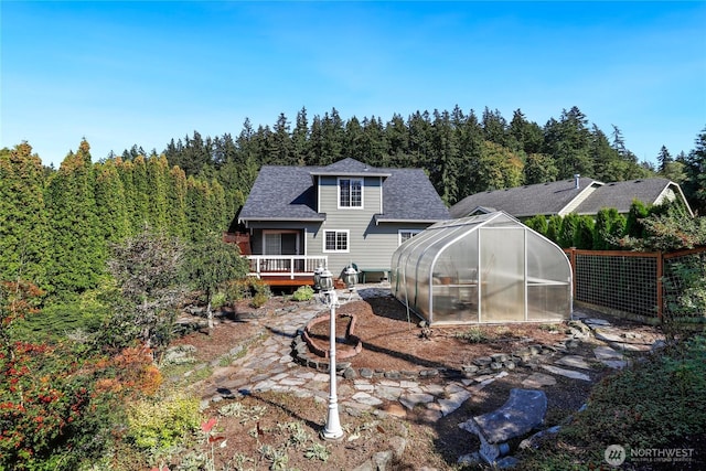 rear view of property featuring an outbuilding, fence, roof with shingles, a wooden deck, and a greenhouse