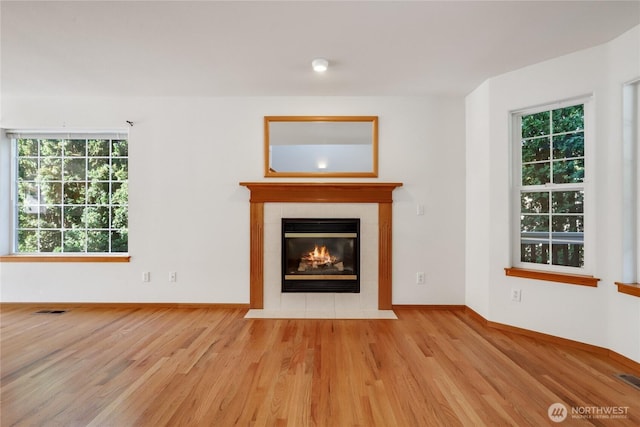 unfurnished living room featuring visible vents, a tile fireplace, baseboards, and wood finished floors