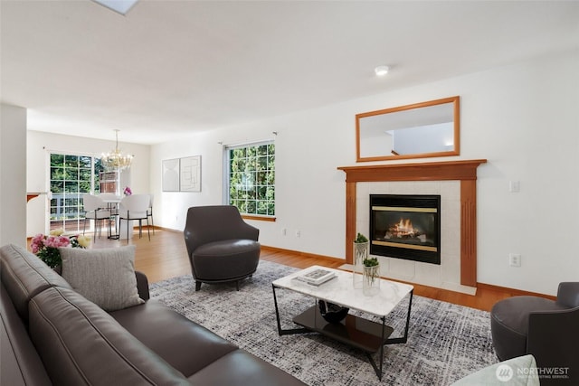 living room featuring baseboards, wood finished floors, a tiled fireplace, and a notable chandelier