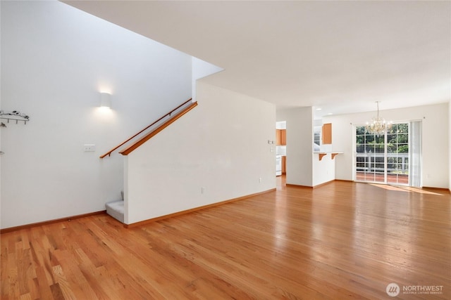 unfurnished living room featuring baseboards, stairway, light wood-style floors, and a notable chandelier