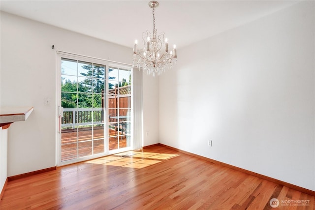 empty room with baseboards, wood finished floors, and an inviting chandelier
