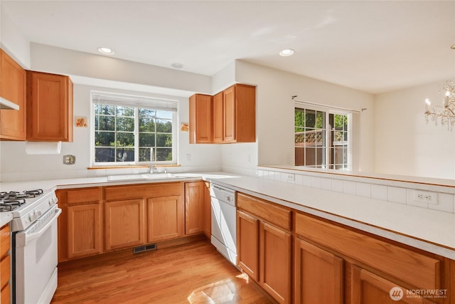 kitchen with light countertops, a sink, a chandelier, white appliances, and light wood-style floors