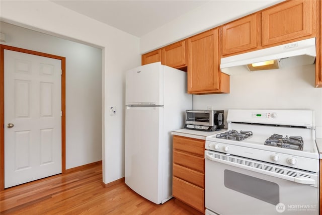 kitchen with light countertops, light wood finished floors, under cabinet range hood, white appliances, and a toaster
