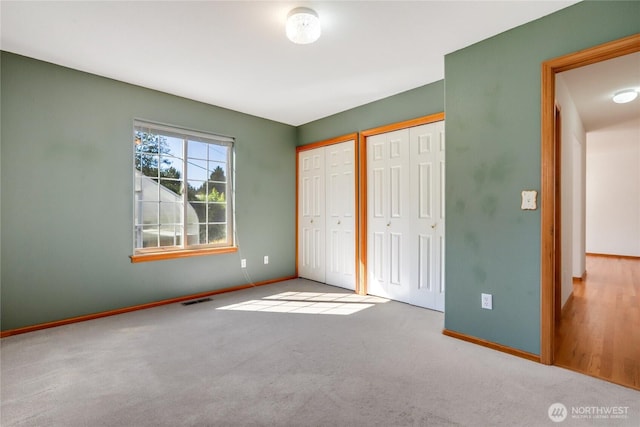 unfurnished bedroom with baseboards, carpet floors, visible vents, and two closets