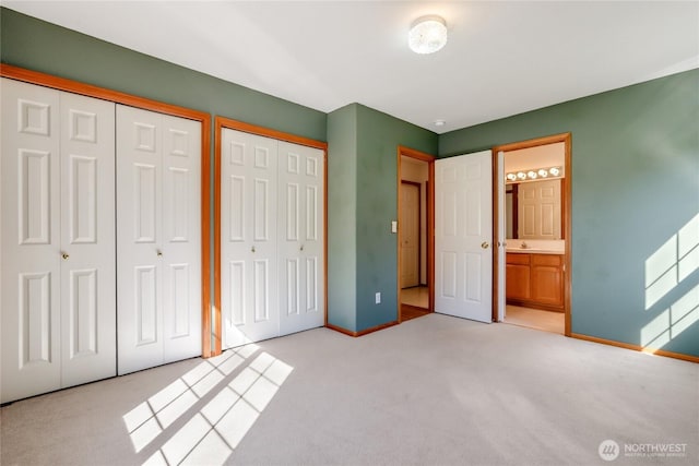 unfurnished bedroom with baseboards, multiple closets, ensuite bath, and light colored carpet