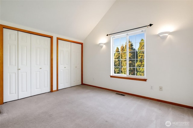 unfurnished bedroom with lofted ceiling, baseboards, visible vents, two closets, and carpet