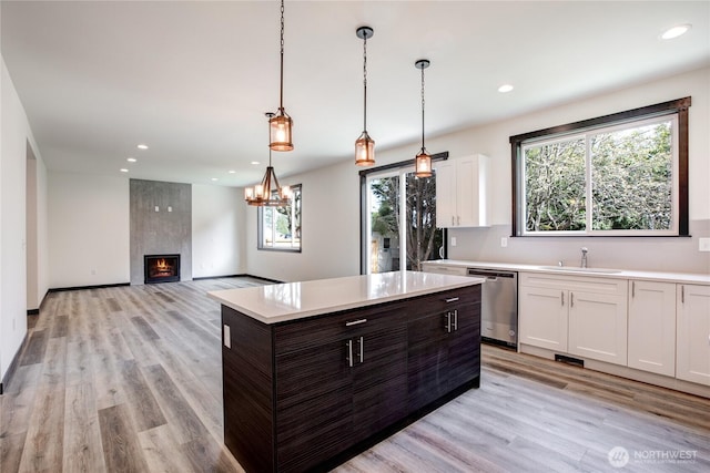 kitchen featuring stainless steel dishwasher, a sink, white cabinets, and light countertops