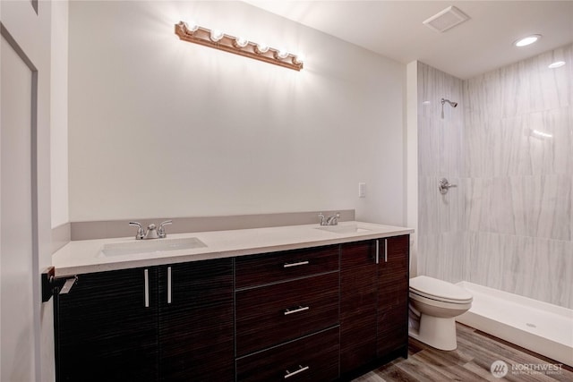 full bath with a sink, wood finished floors, toilet, and tiled shower
