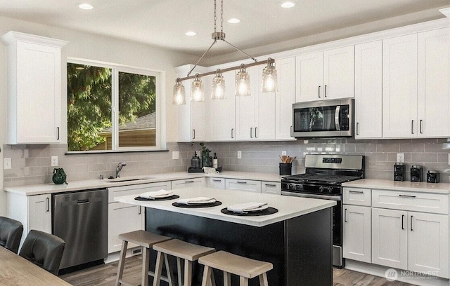 kitchen featuring appliances with stainless steel finishes, a sink, light countertops, a kitchen bar, and backsplash