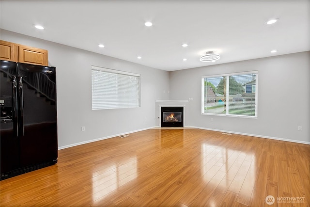 unfurnished living room with baseboards, a fireplace with flush hearth, light wood-style flooring, and recessed lighting