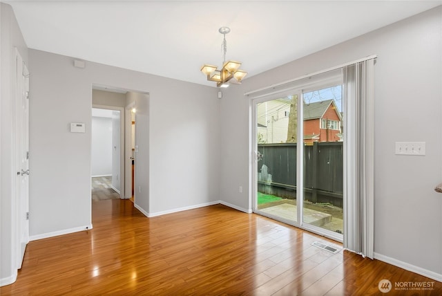 unfurnished room featuring visible vents, a notable chandelier, baseboards, and wood finished floors