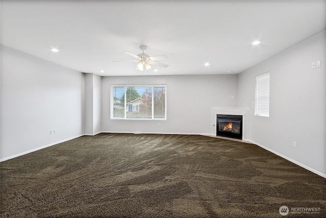 unfurnished living room featuring baseboards, recessed lighting, dark colored carpet, and a glass covered fireplace