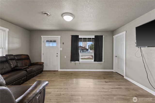living room with light wood-type flooring, baseboards, visible vents, and a textured ceiling