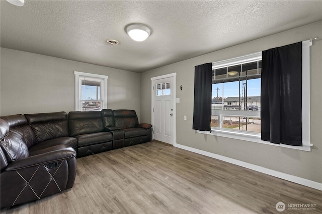 living room featuring a textured ceiling, wood finished floors, baseboards, and visible vents