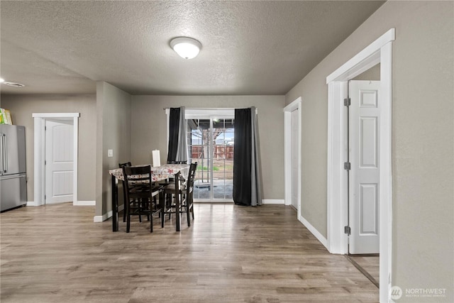 dining room with light wood finished floors, baseboards, and a textured ceiling