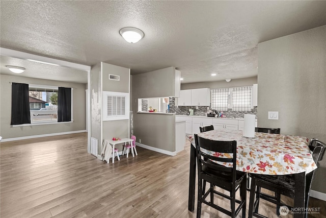 dining area featuring a textured ceiling, light wood finished floors, baseboards, and visible vents
