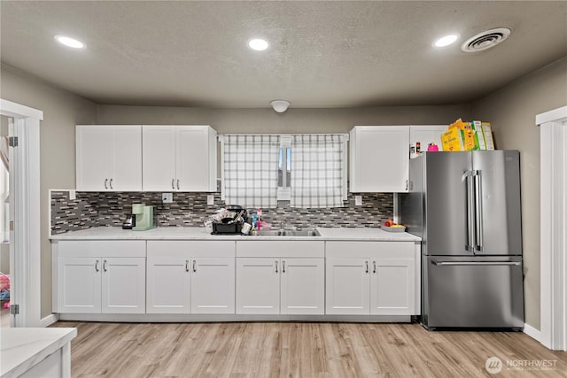 kitchen with light wood-style flooring, white cabinetry, high quality fridge, visible vents, and light countertops