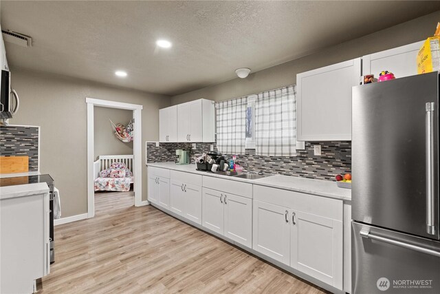kitchen featuring light countertops, white cabinetry, light wood-style floors, decorative backsplash, and stainless steel appliances