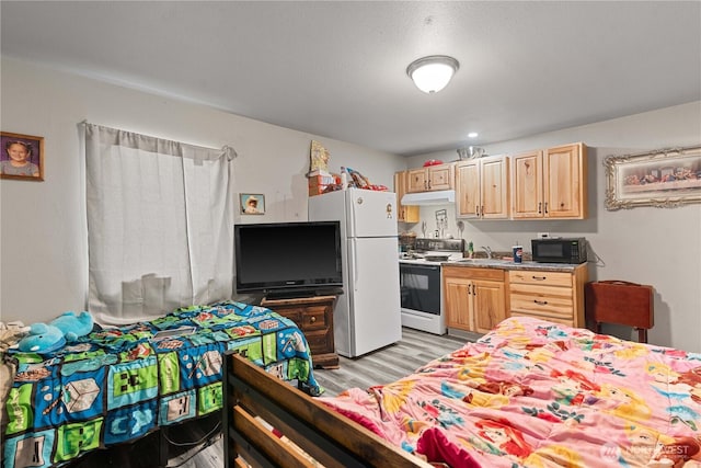 kitchen with freestanding refrigerator, black microwave, light wood-style flooring, light brown cabinetry, and range with electric stovetop