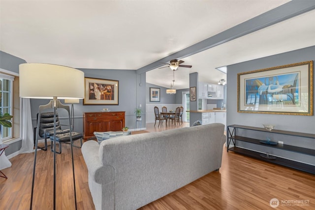 living area with ceiling fan, baseboards, vaulted ceiling with beams, and wood finished floors
