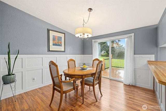 dining room with a decorative wall, vaulted ceiling, light wood-type flooring, and an inviting chandelier