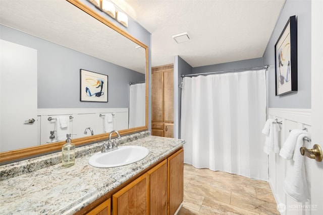 bathroom featuring a textured ceiling, curtained shower, wainscoting, and vanity