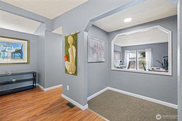 hall featuring visible vents, baseboards, and wood finished floors