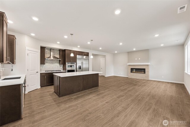 11519 SE 84th St Unit 44, Newcastle, WA 98056 - kitchen featuring wall chimney exhaust hood, appliances with stainless steel finishes, dark brown cabinetry, a center island, and wood finished floors
