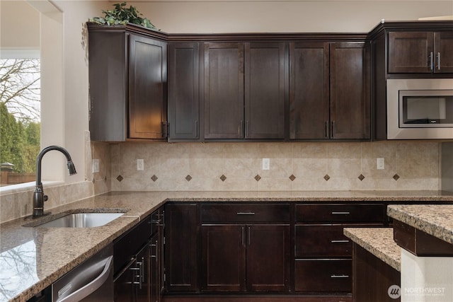 kitchen with light stone counters, dark brown cabinetry, a sink, tasteful backsplash, and stainless steel appliances