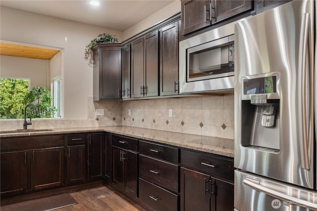 kitchen with a sink, light stone countertops, appliances with stainless steel finishes, decorative backsplash, and dark brown cabinets