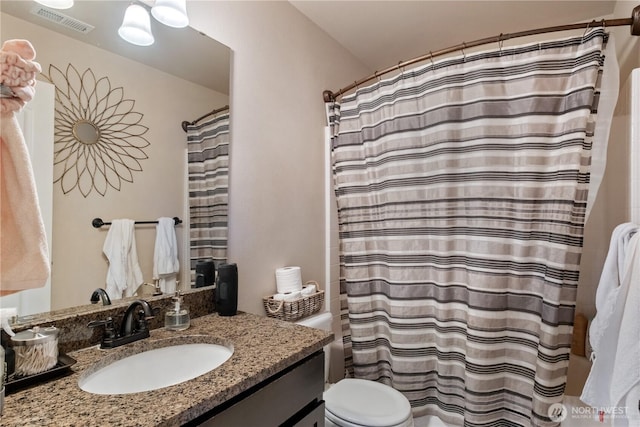 bathroom with toilet, vanity, shower / bath combo with shower curtain, and visible vents