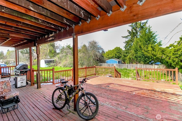 wooden terrace featuring an outdoor structure, grilling area, and fence