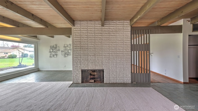 unfurnished living room featuring a brick fireplace, baseboards, stone tile flooring, beam ceiling, and wooden ceiling