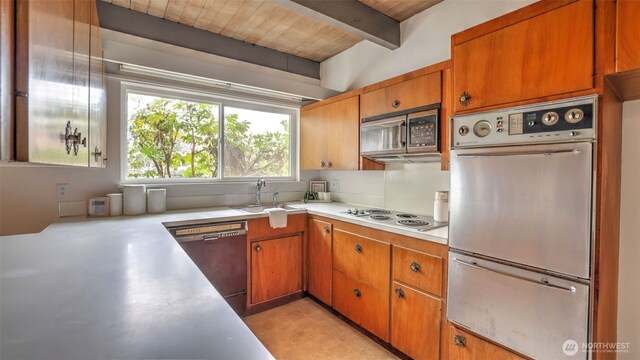 kitchen with light countertops, a sink, brown cabinets, stainless steel appliances, and beamed ceiling