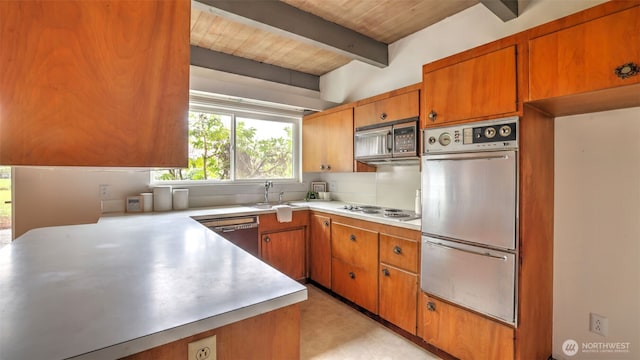 kitchen with a sink, stainless steel appliances, brown cabinetry, and beamed ceiling
