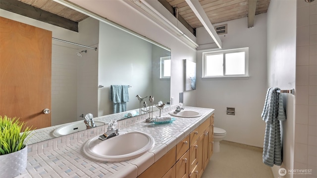 full bathroom with beamed ceiling, toilet, and a sink