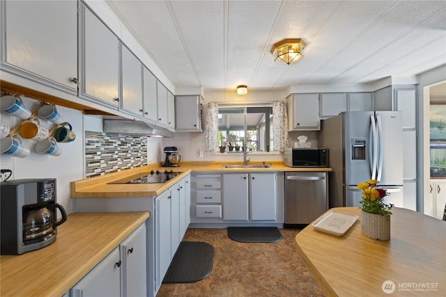 kitchen with a sink, backsplash, appliances with stainless steel finishes, a textured ceiling, and under cabinet range hood