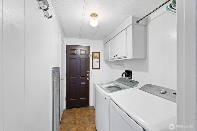 clothes washing area with cabinet space, a textured ceiling, and washer and clothes dryer