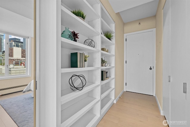 corridor with baseboards, a baseboard heating unit, and light wood-type flooring