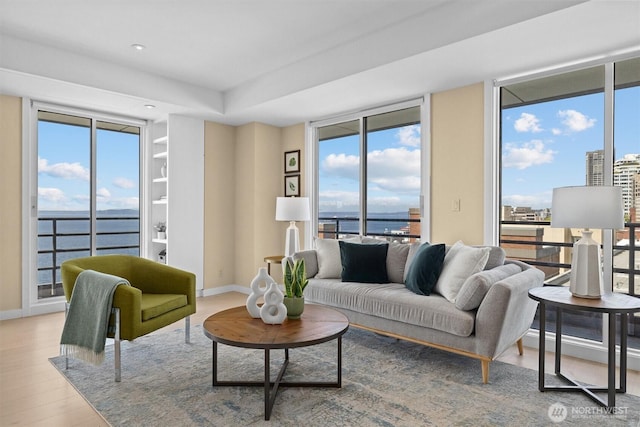living area featuring a healthy amount of sunlight, baseboards, a water view, and wood finished floors