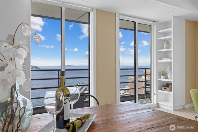 dining space with expansive windows, a water view, and built in shelves