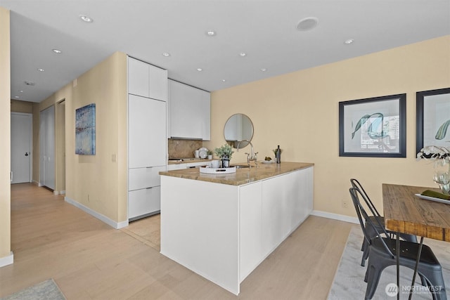 kitchen with light wood-style floors, white cabinetry, baseboards, a peninsula, and modern cabinets