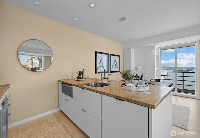 kitchen with a peninsula, baseboards, modern cabinets, white cabinetry, and a sink