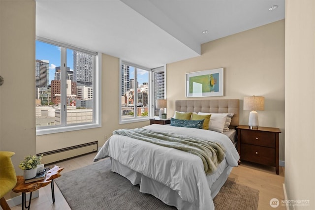 bedroom with a city view, a baseboard heating unit, and light wood finished floors