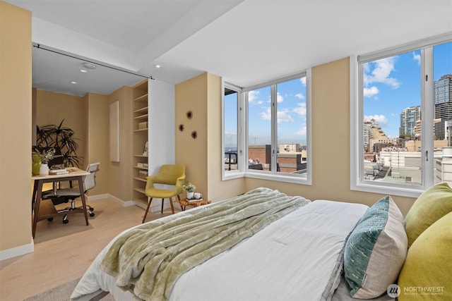 bedroom with a walk in closet, baseboards, a view of city, light wood-style floors, and recessed lighting