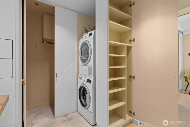 washroom featuring baseboards, stacked washer / drying machine, and laundry area