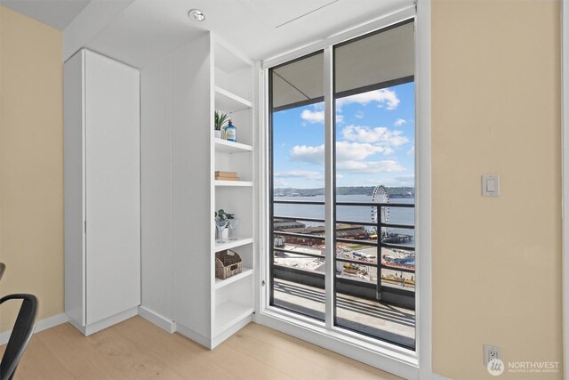 interior space with light wood-style floors, a water view, a wall of windows, and baseboards
