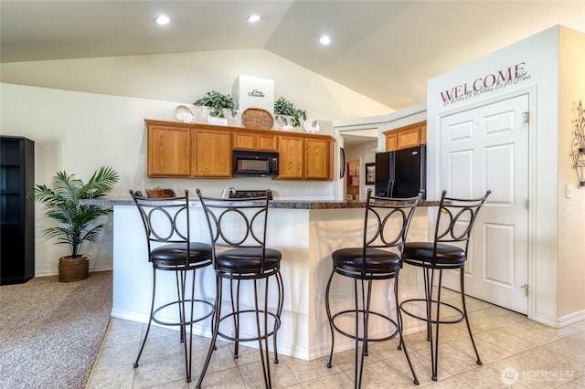 kitchen with dark countertops, a breakfast bar area, vaulted ceiling, and black appliances