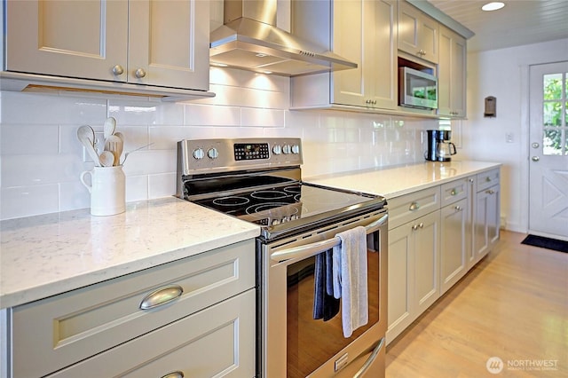 987 Cavalero Rd, Camano Island, WA 98282 - kitchen with tasteful backsplash, light stone counters, light wood-style floors, appliances with stainless steel finishes, and wall chimney range hood